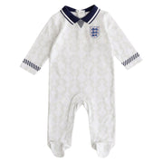 A white England Football 1990 retro baby sleepsuit with a geometric pattern, featuring the England Football national team badge on the chest and navy blue collar and cuff details.